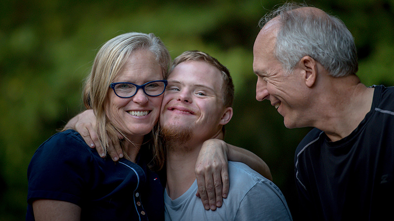 A woman embracing a teenager, with a man looking on.