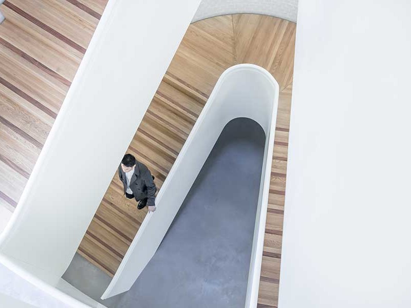 Looking down a modern stairwell with inlaid wood risers, and cement floors.