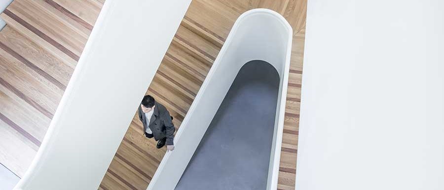 Looking down a modern stairwell with inlaid wood risers, and cement floors.