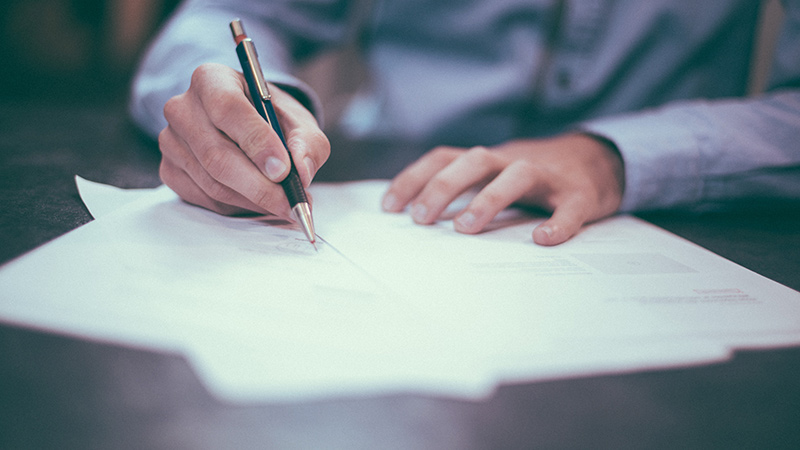 A business person writing on a report with a pen.