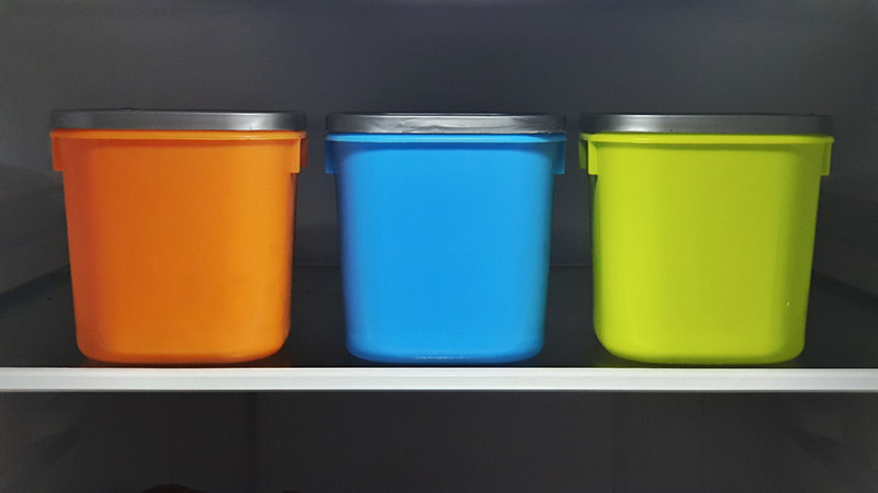 Three lidded containers, orange, blue and green, on a shelf.