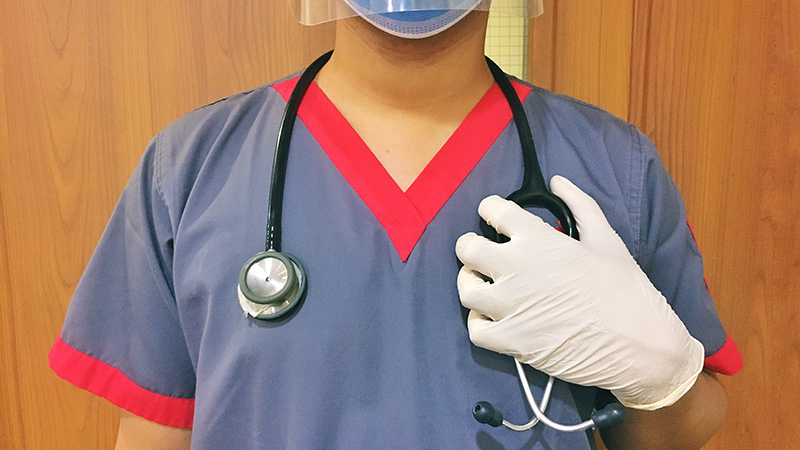 A healthcare professional in scrubs wearing gloves and a mask.