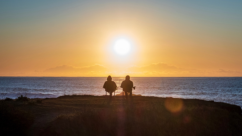 Two seated people watching the sunset at the beach.