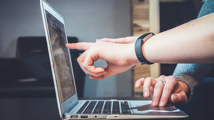 Two people reviewing documents on a laptop screen.