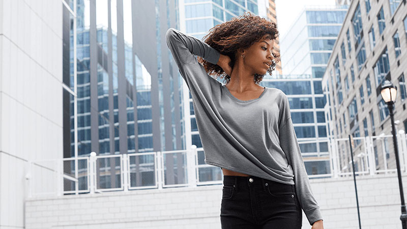 Woman in a long sleeve grey t-shirt and black jeans, on a outdoor city deck.