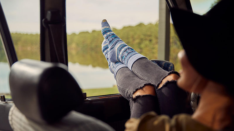 Woman in a car, relaxing with her feet in socks, up on the window ledge.