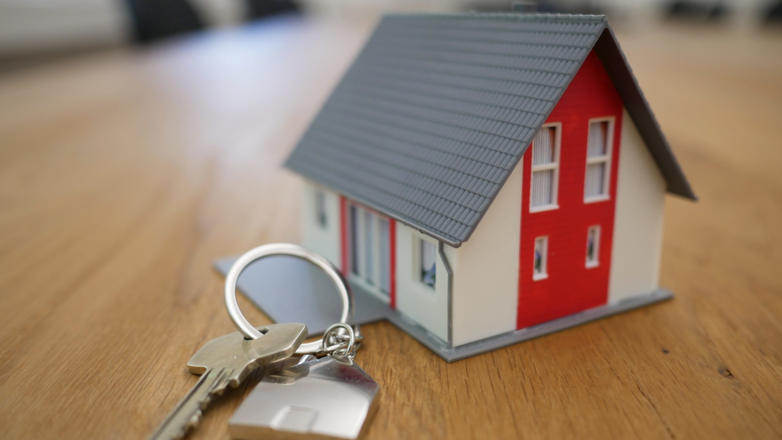 A toy house on a wooden conference table, with a set of keys.