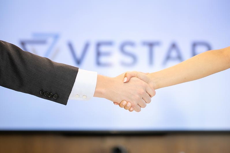 Man and woman shaking hands in front of Vestar logo