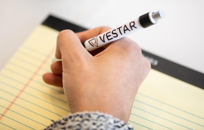 Person writing with Vestar branded pen on yellow pad